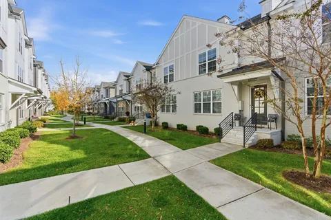 a view of a white house next to a yard with big trees