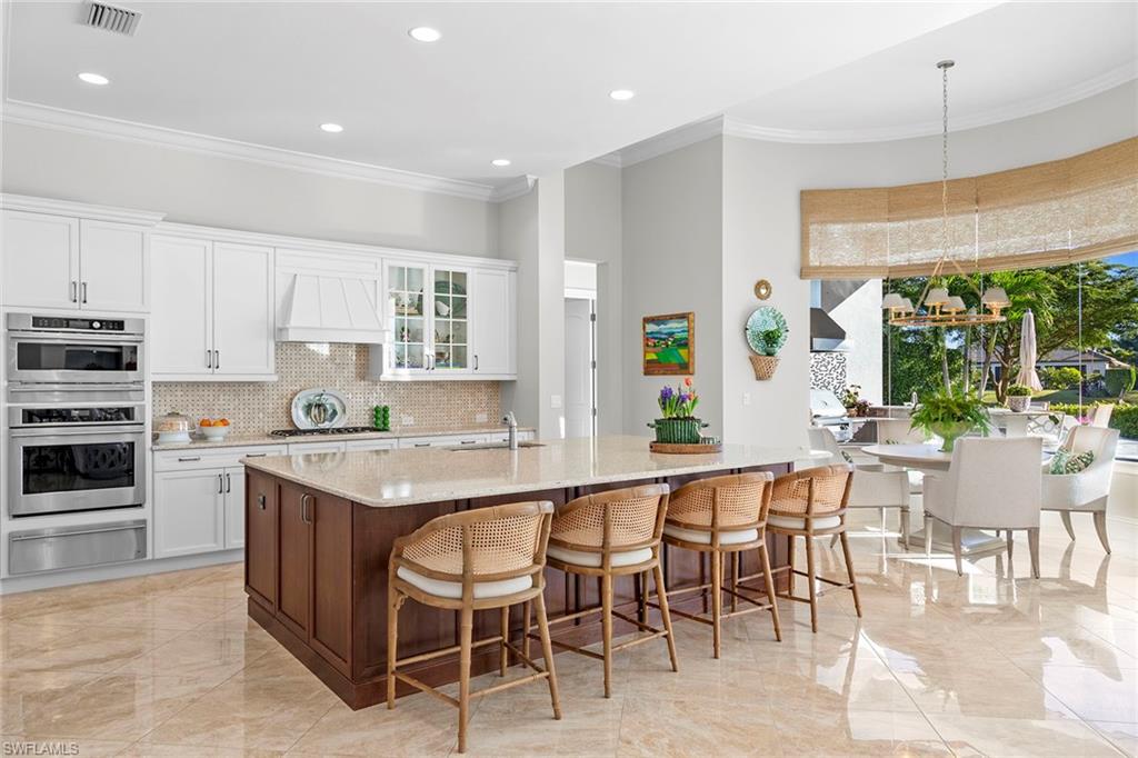4170 Cortland Way Naples, FL 34119 - Photo 11 of 41 Kitchen with glass insert cabinets, white cabinetry, a breakfast bar area, ornamental molding, and light stone counters