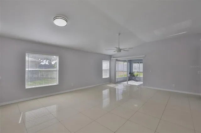 an empty room with chandelier fan and windows