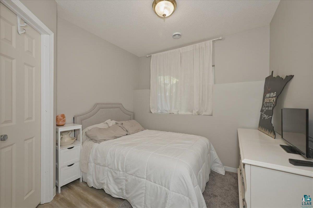 47 Amy Lane Esko, MN 55733 - Photo 16 of 33 Bedroom featuring neutral wall colors, a window with sheer white curtains, and wood-finish flooring transitioning to carpeting