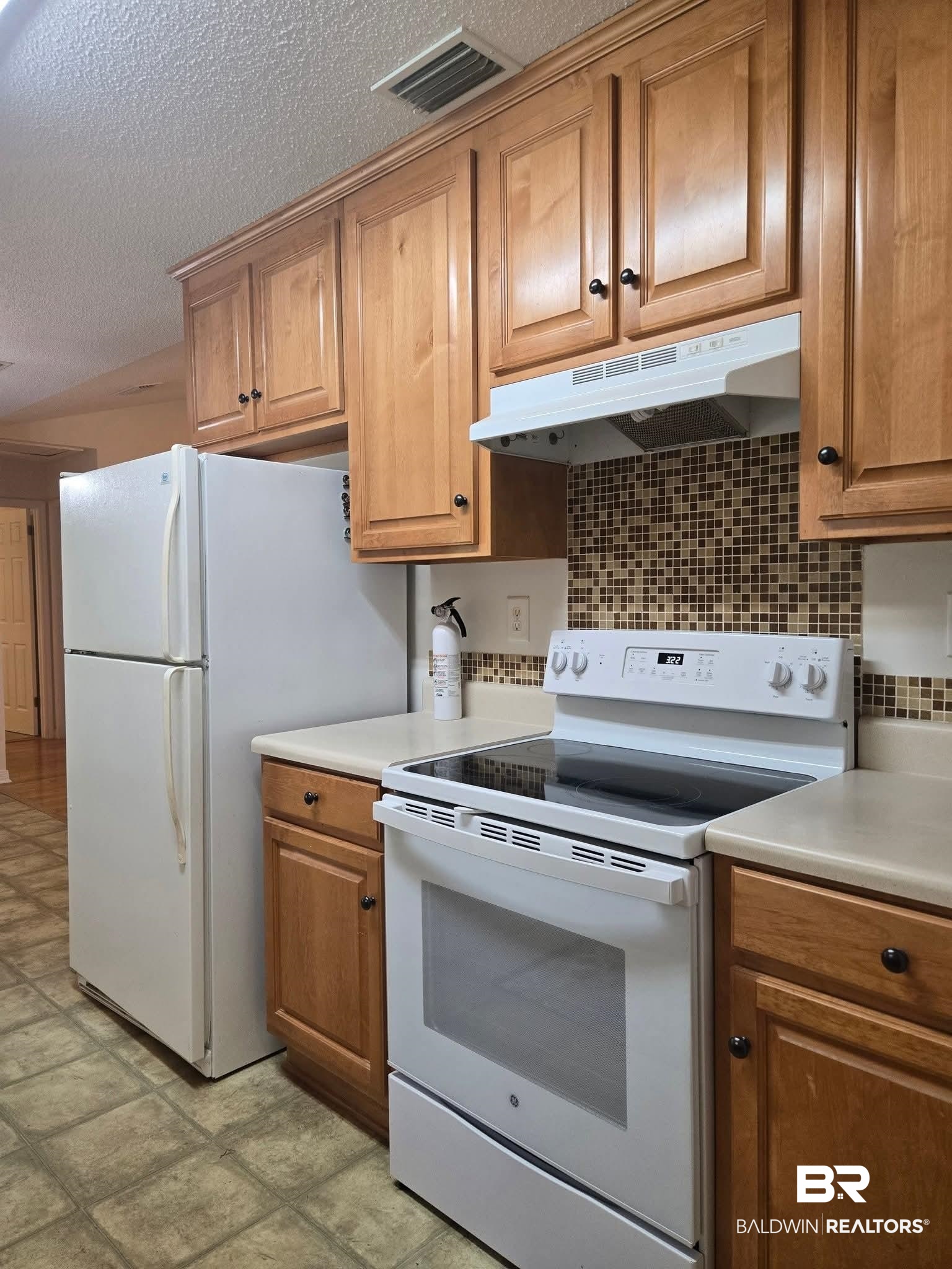 2554 Riverside Drive Mobile, AL 36605 - Photo 5 of 43 Kitchen featuring white appliances, under cabinet range hood, brown cabinetry, light countertops, and a textured ceiling
