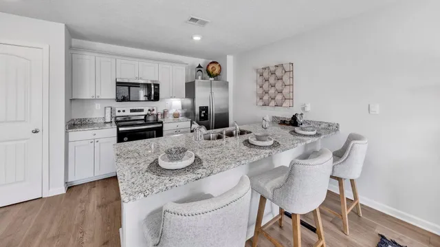 a kitchen with stainless steel appliances granite countertop a sink stove and white cabinets with wooden floor