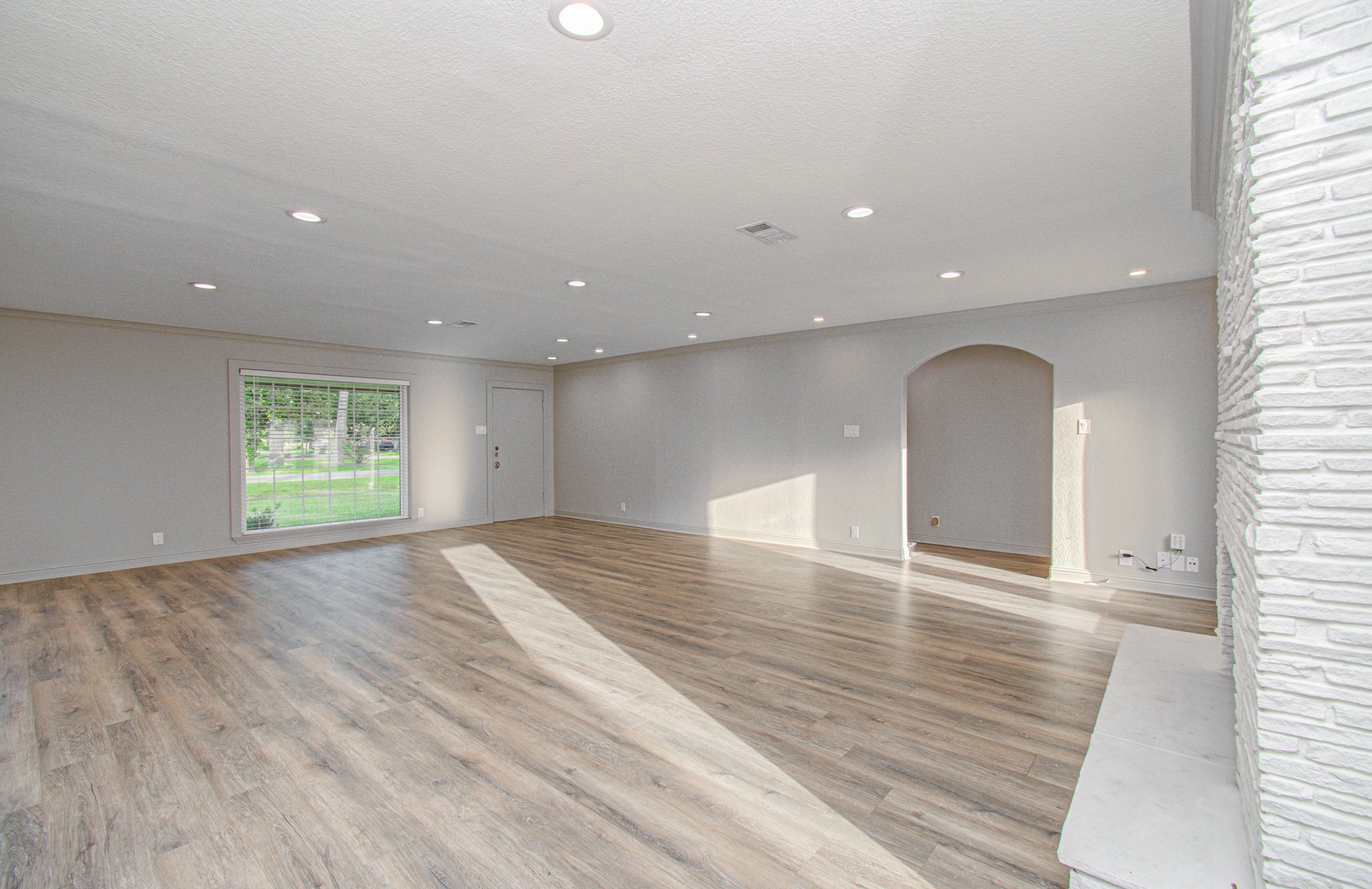 1801 Benbow Way Houston, TX 77080 - Photo 6 of 32 This spacious living room features elegant wood flooring, recessed lighting, and a large window providing ample natural light. The room includes a unique arched doorway and a textured accent wall, creating a modern and inviting atmosphere.