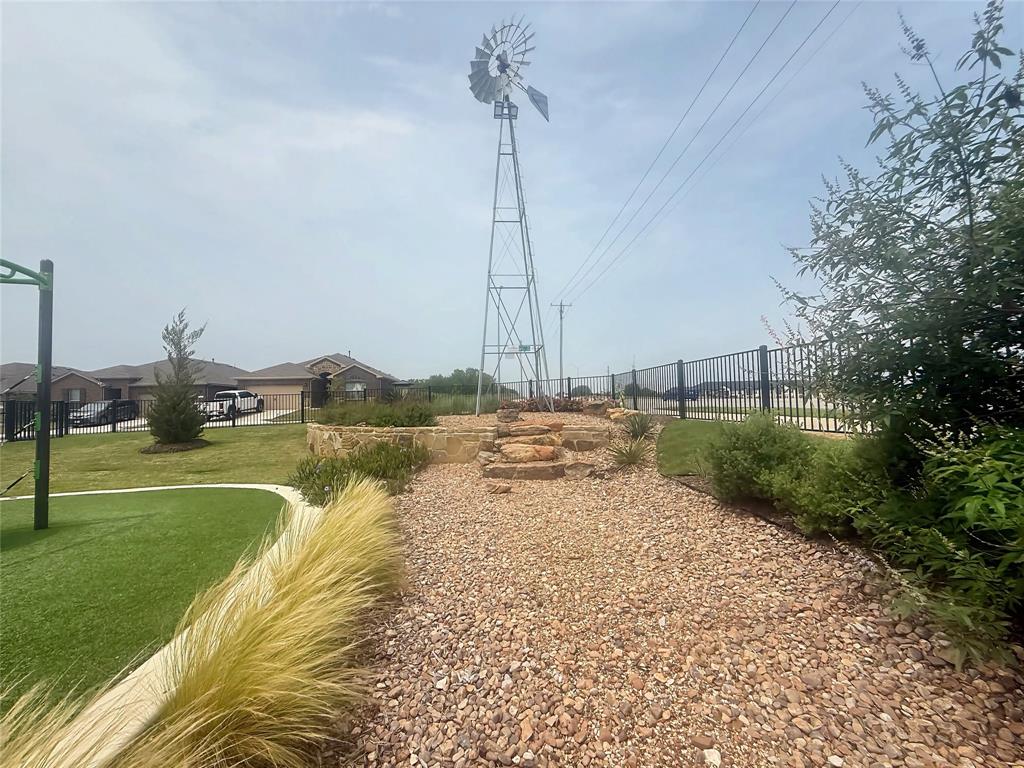 9604 Cherryville Road Fort Worth, TX 76108 - Photo 38 of 40 Outdoor area featuring a decorative windmill, natural stone landscaping, gravel pathways, and a black metal fence