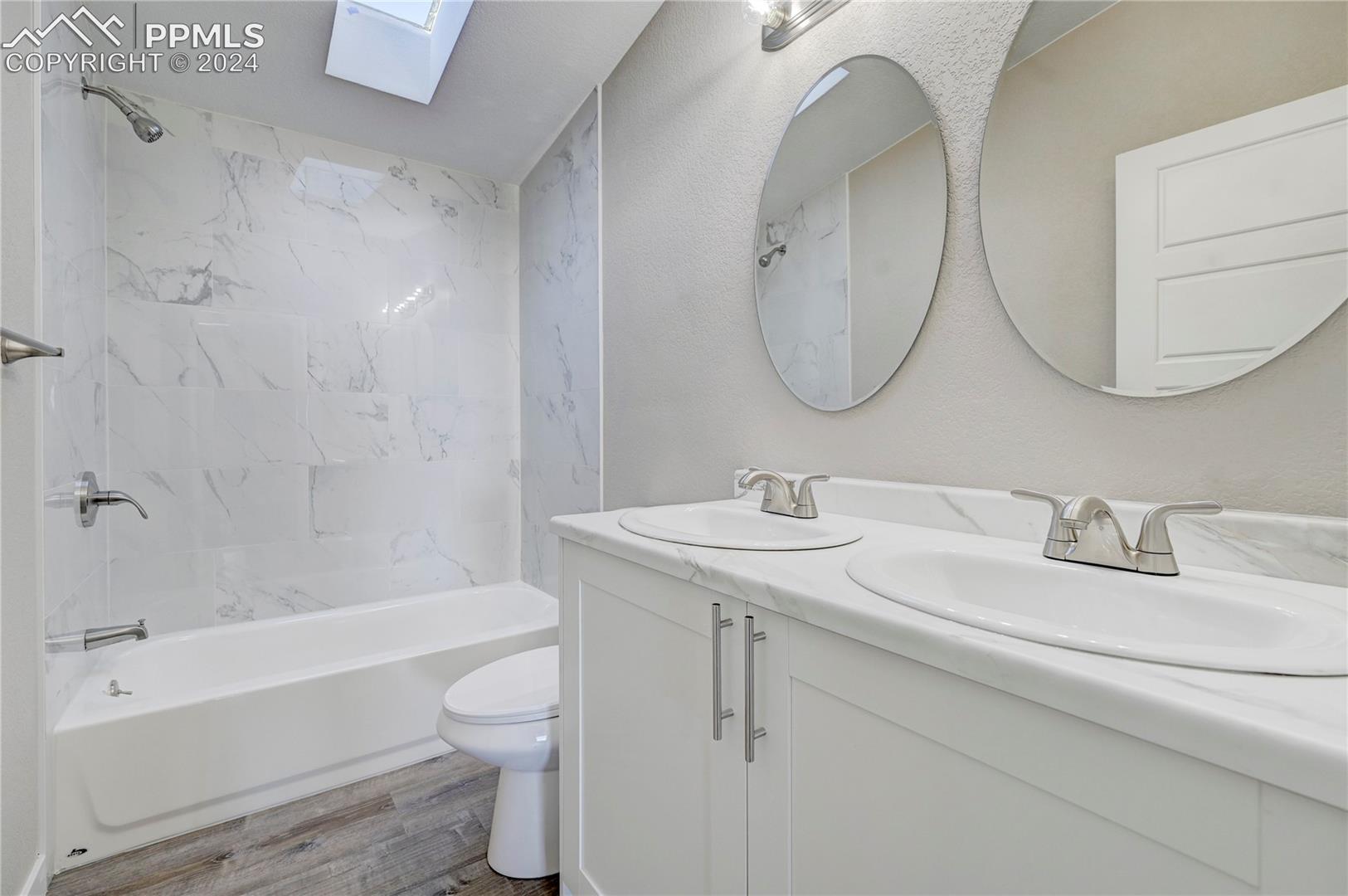6605 Rio Road Peyton, CO 80831 - Photo 24 of 45 Full bathroom featuring vanity, a skylight, hardwood / wood-style flooring, tiled shower / bath combo, and toilet