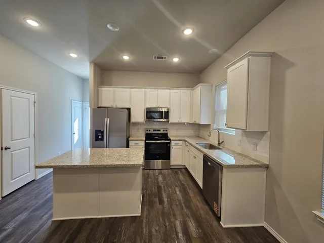 a large kitchen with stainless steel appliances kitchen island granite countertop a stove a sink a refrigerator and white cabinets with wooden floor