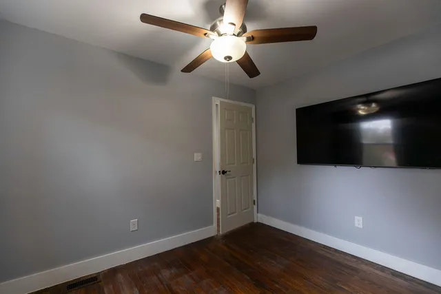 an empty room with wooden floor and fan