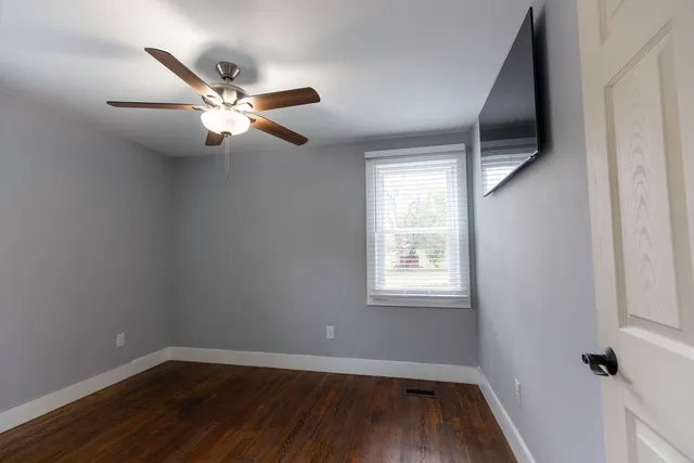 an empty room with wooden floor fan and windows