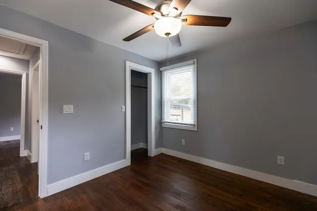 an empty room with wooden floor chandelier fan and windows
