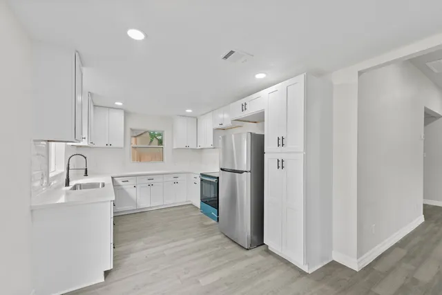 a large white kitchen with a refrigerator a sink a stove and white cabinets