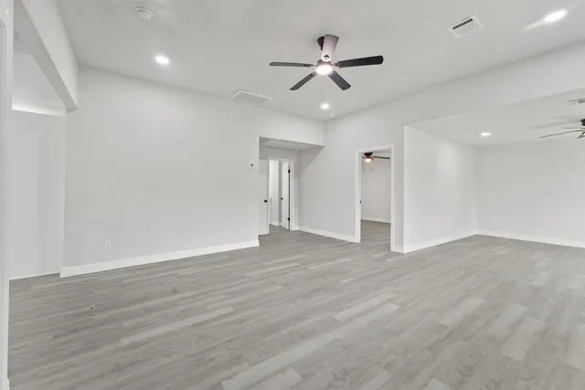 a view of an empty room with wooden floor and a ceiling fan
