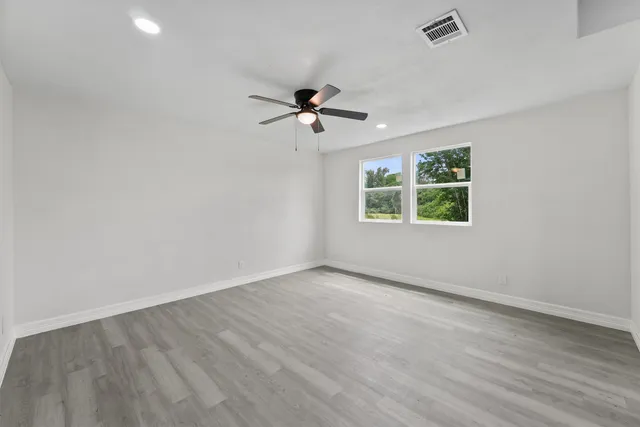 an empty room with wooden floor ceiling fan and windows