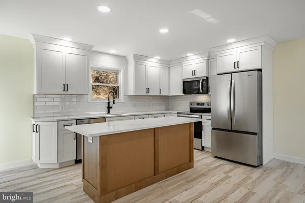 a kitchen with stainless steel appliances granite countertop a sink stove a refrigerator and white cabinets with wooden floor
