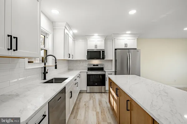 a large kitchen with kitchen island a sink dishwasher a refrigerator and white cabinets with wooden floor