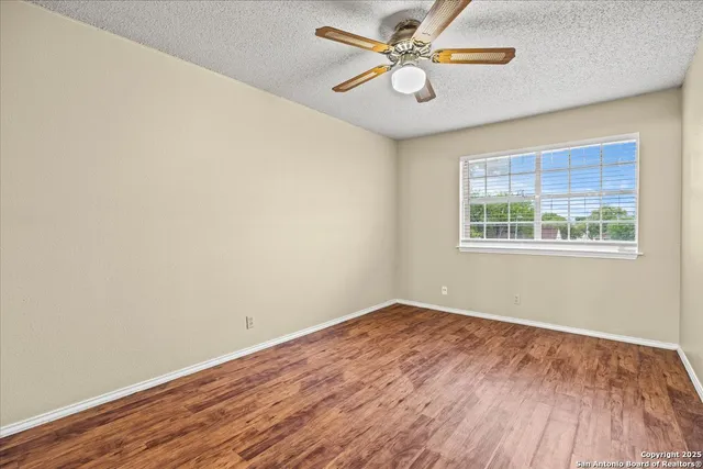 a view of empty room with wooden floor and fan