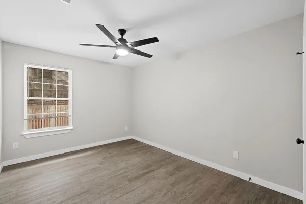 an empty room with wooden floor fan and windows