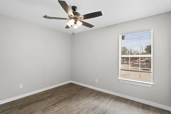 an empty room with wooden floor fan and windows
