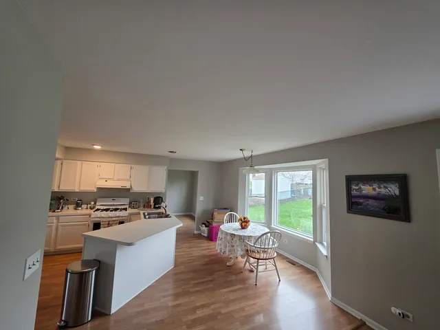 a large open kitchen with stainless steel appliances granite countertop a stove a sink a refrigerator white cabinets and wooden floor