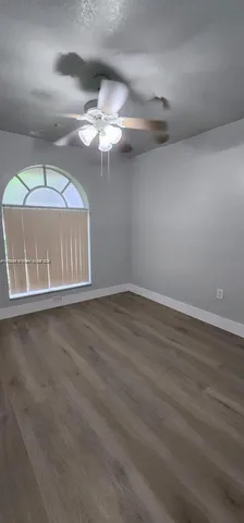 an empty room with wooden floor chandelier fan and windows