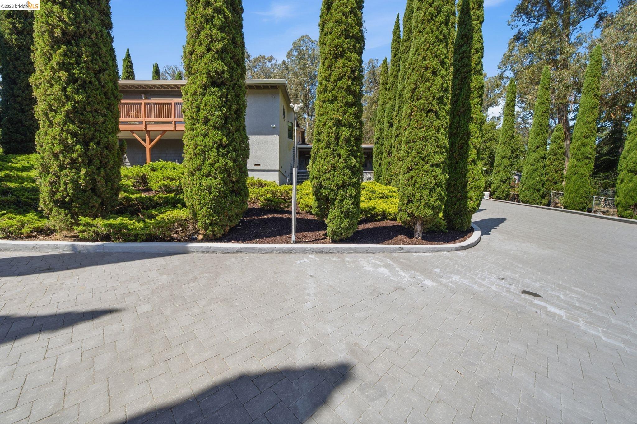 11133 Golf Links Road Oakland, CA 94605 - Photo 53 of 57 Herringbone pattern paver driveway with lush landscaping and mature columnar evergreen trees