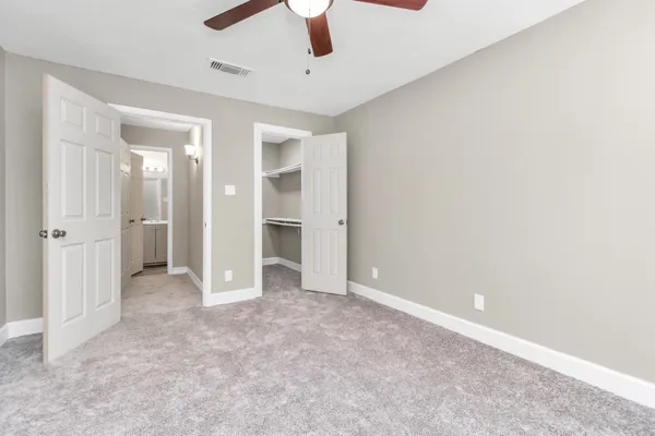 an empty room with chandelier fan and kitchen view