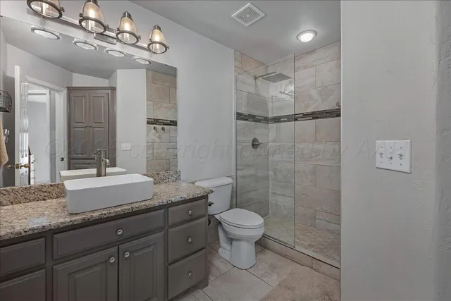 a spacious bathroom with a granite countertop sink a toilet a mirror and shower