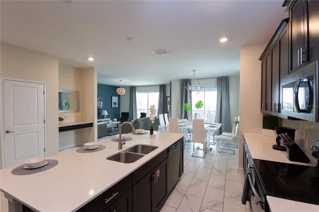 a dining hall with stainless steel appliances kitchen island granite countertop a refrigerator a sink a stove and white cabinets with wooden floor