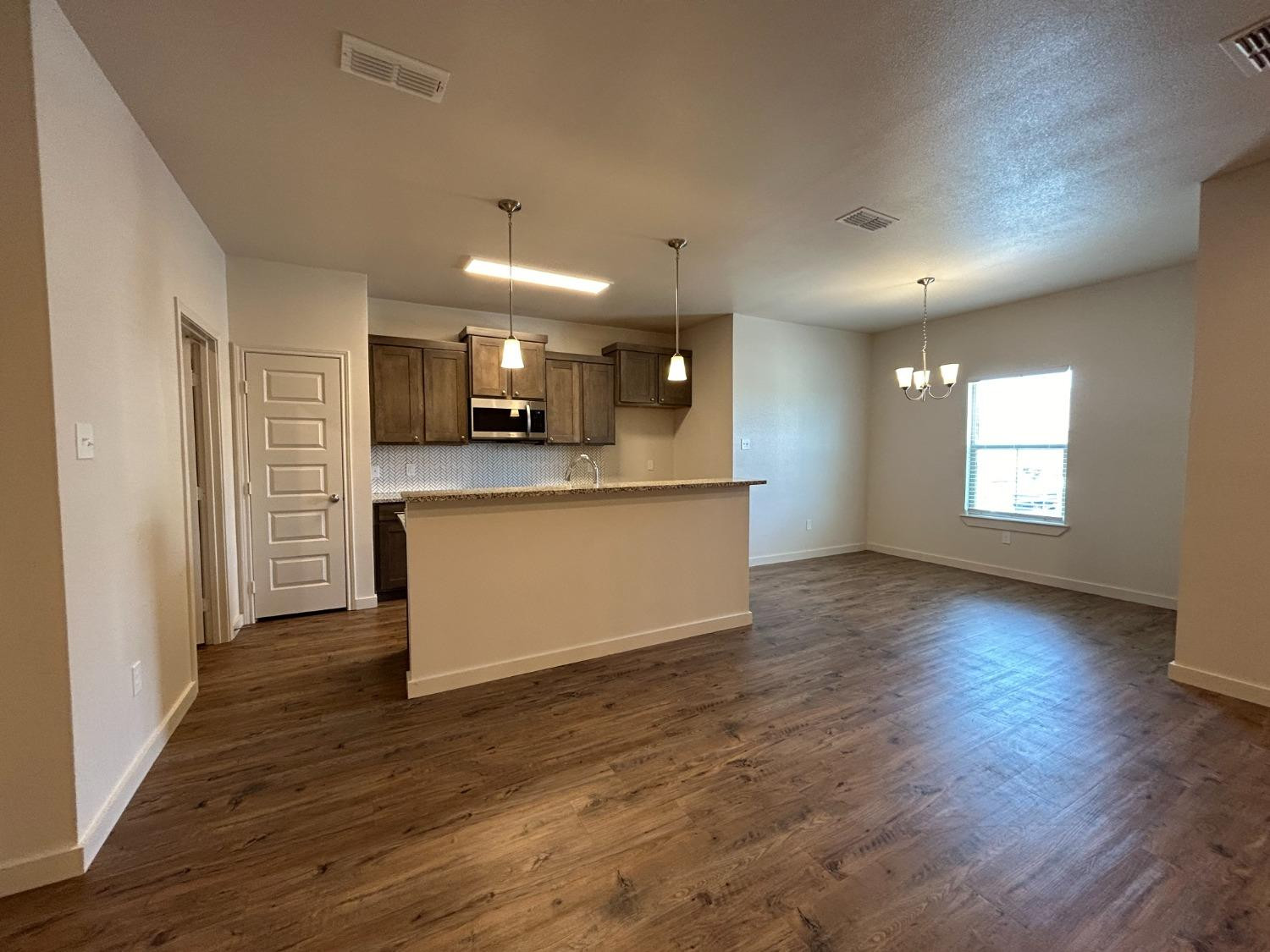 2603 135th Street Lubbock, TX 79423 - Photo 4 of 12 an empty room with wooden floor and kitchen view