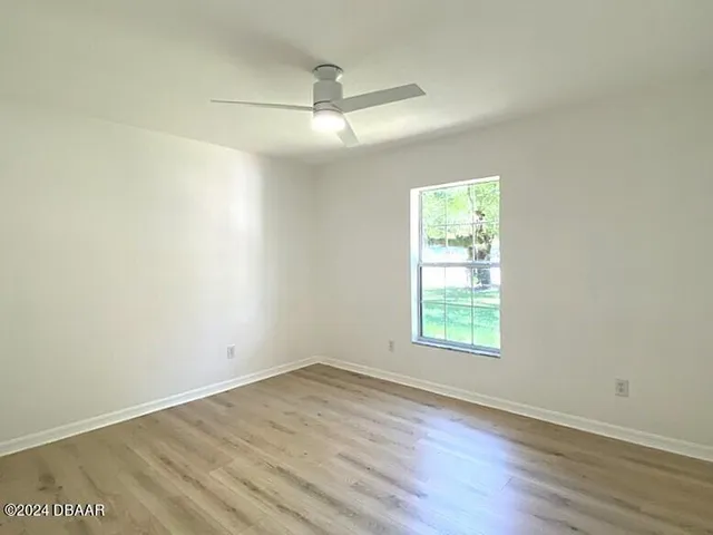 an empty room with wooden floor chandelier fan and windows