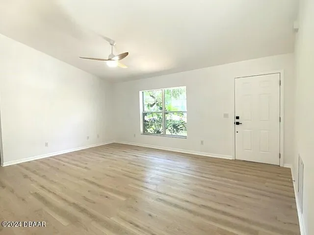 an empty room with wooden floor chandelier fan and windows