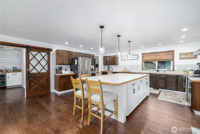 a large kitchen with stainless steel appliances kitchen island granite countertop a stove a sink a refrigerator and a dining table with wooden floor