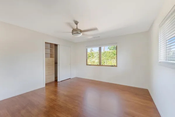 an empty room with wooden floor chandelier fan and windows
