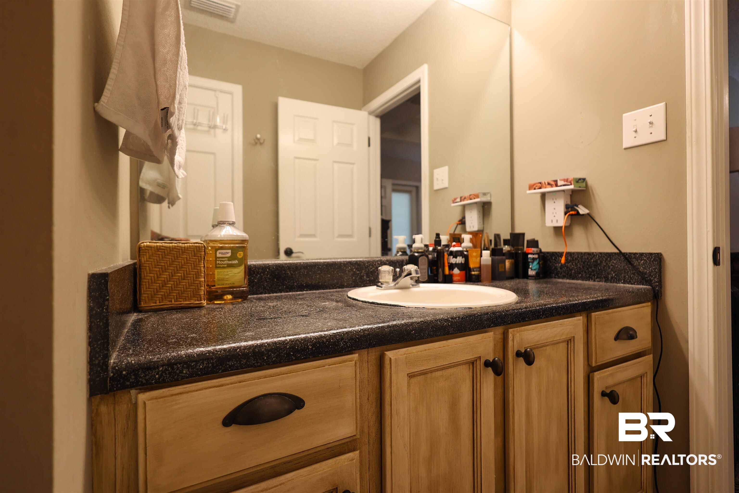 7790 Audubon Drive Foley, AL 36535 - Photo 22 of 39 Bathroom vanity featuring a speckled dark countertop, an integrated sink basin, and a light wood-finish cabinet with dark hardware