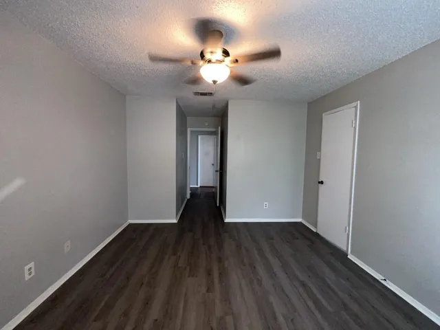 a view of an empty room with wooden floor and a ceiling fan