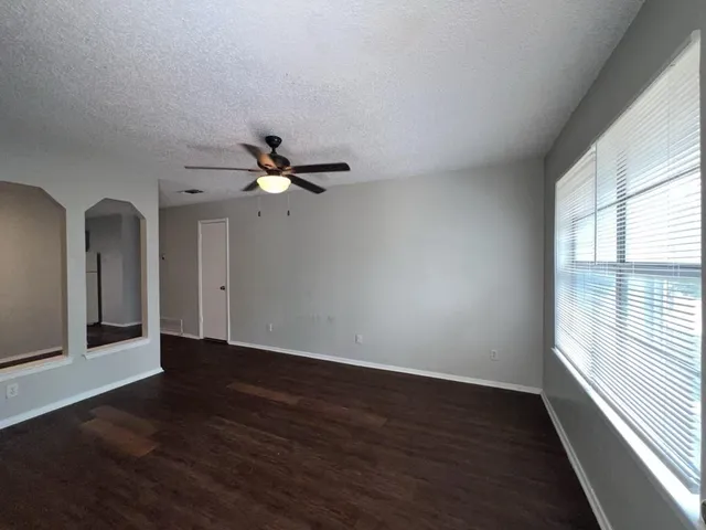 an empty room with wooden floor fan and windows