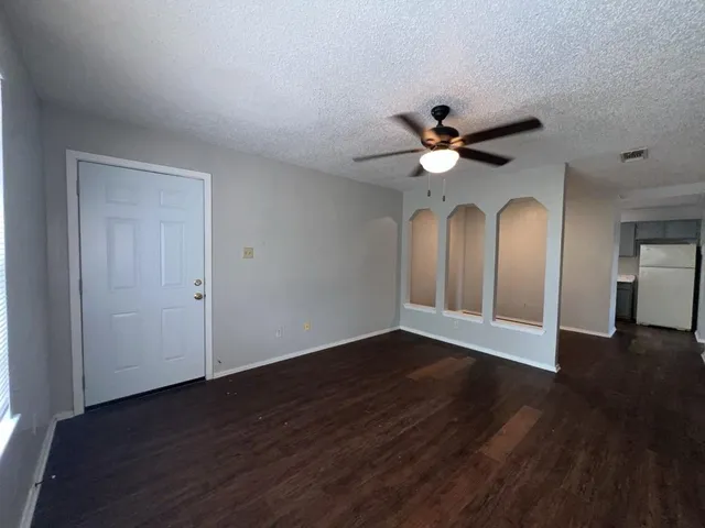 a view of an empty room with chandelier fan and wooden floor