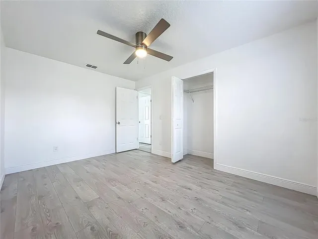 an empty room with wooden floor fan and windows