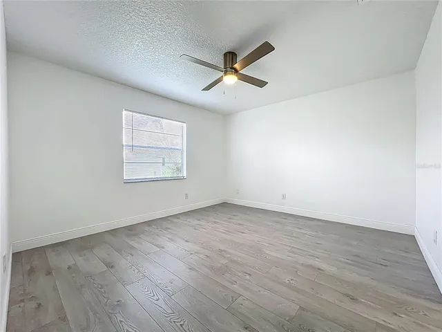 an empty room with wooden floor ceiling fan and windows