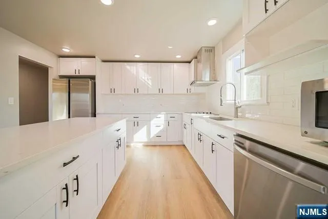 a large white kitchen with a large counter top space a sink a refrigerator and white cabinets