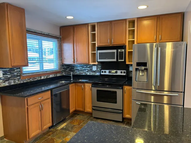 a kitchen with granite countertop stainless steel appliances a refrigerator cabinets and a window