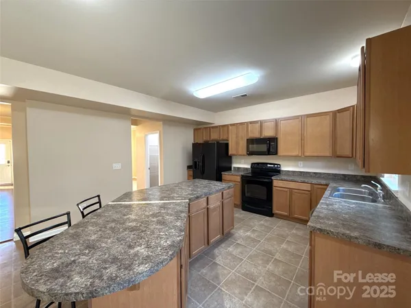 a large kitchen with kitchen island granite countertop a stove top oven a sink a counter space and cabinets