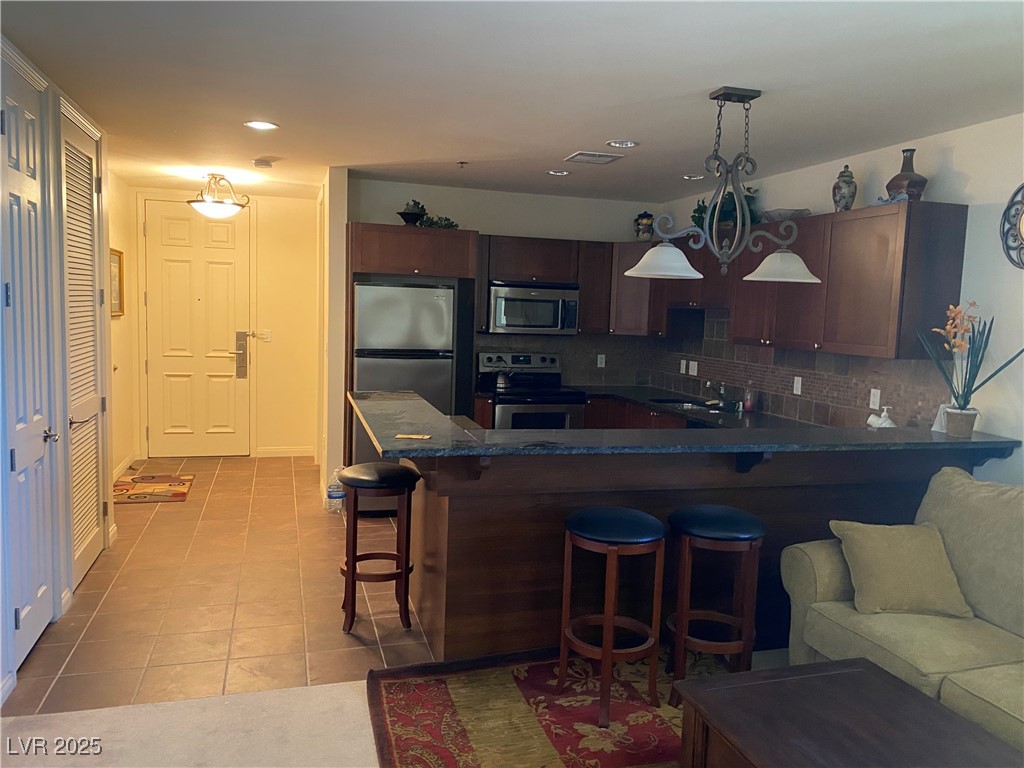 2405 West Serene Avenue, Unit 827 Las Vegas, NV 89123 - Photo 39 of 48 Kitchen with tasteful backsplash, a kitchen breakfast bar, appliances with stainless steel finishes, dark tile patterned floors, and pendant lighting