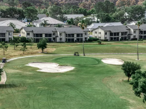 a view of a white house with a swimming pool and lawn chairs under an umbrella