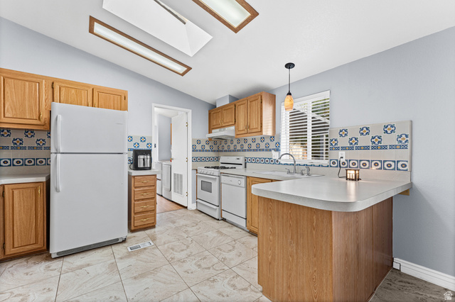 312 Harriger Way Layton, UT 84041 - Photo 18 of 36 Kitchen featuring a breakfast bar, white appliances, wood cabinetry, patterned tile backsplash, and skylights