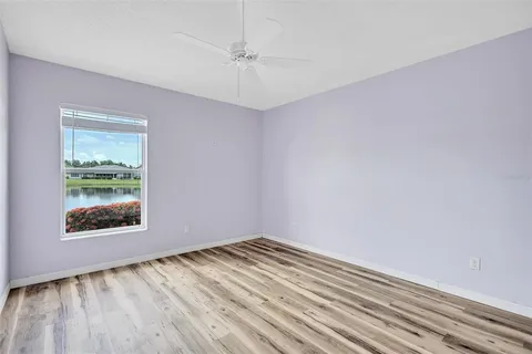 an empty room with wooden floor chandelier fan and windows
