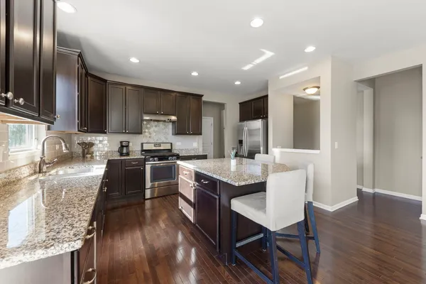 a kitchen with granite countertop stainless steel appliances a sink a stove a refrigerator cabinets and wooden floor