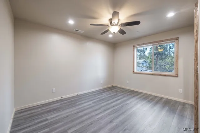an empty room with wooden floor fan and windows