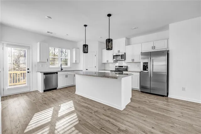 a kitchen with stainless steel appliances kitchen island granite countertop a refrigerator a sink dishwasher a stove and white countertops with wooden floor