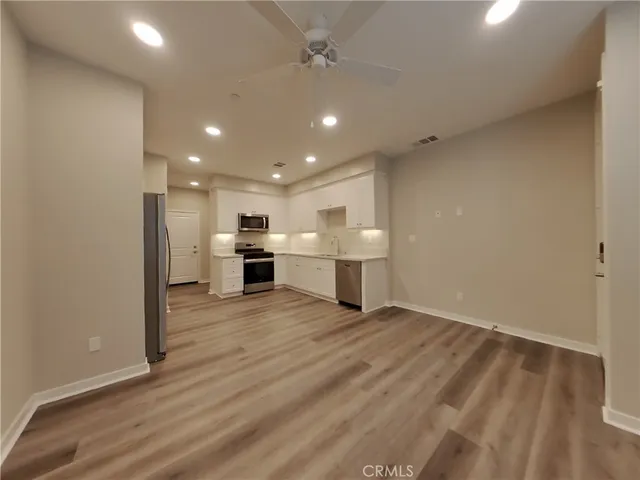 an empty room with wooden floor kitchen electric appliances and windows