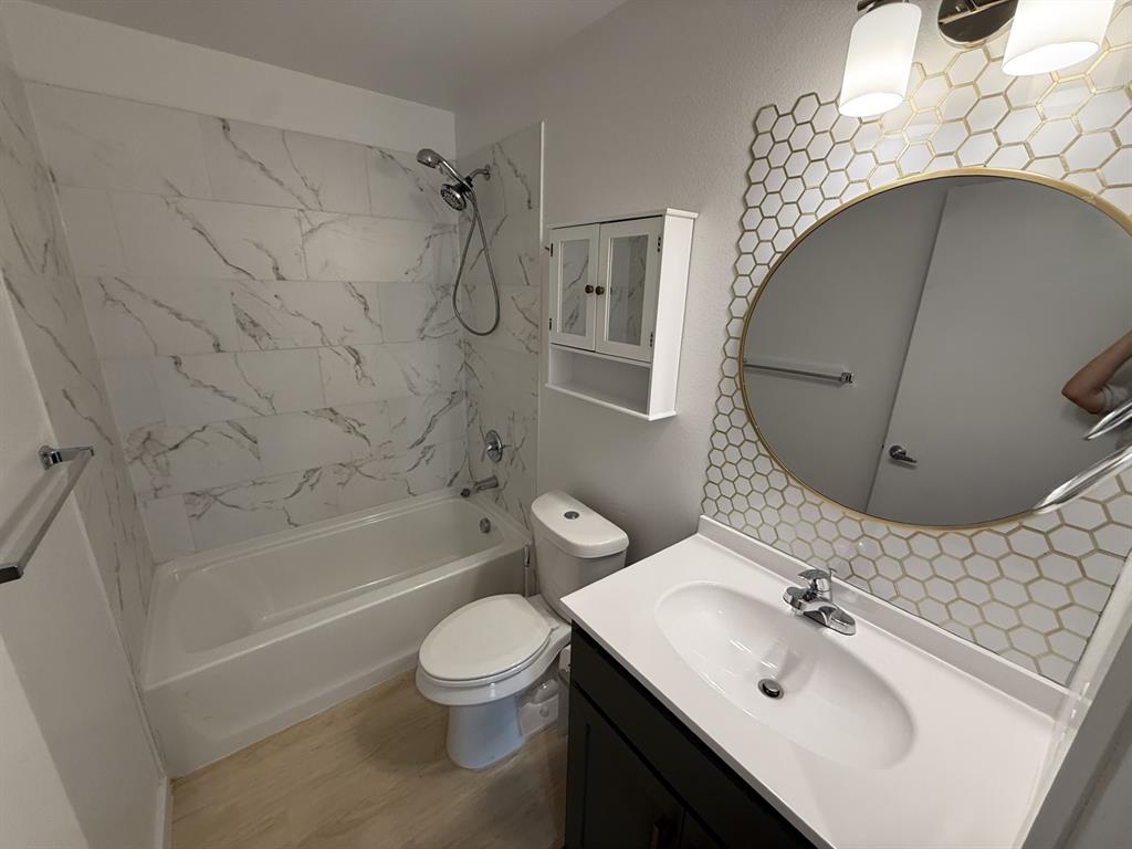 505 Thomas Street Terrell, TX 75160 - Photo 34 of 38 Bathroom featuring a white bathtub with a tile surround, a built-in toilet, a vanity with a white countertop and integrated sink, a framed round mirror, and a hexagon tile backsplash